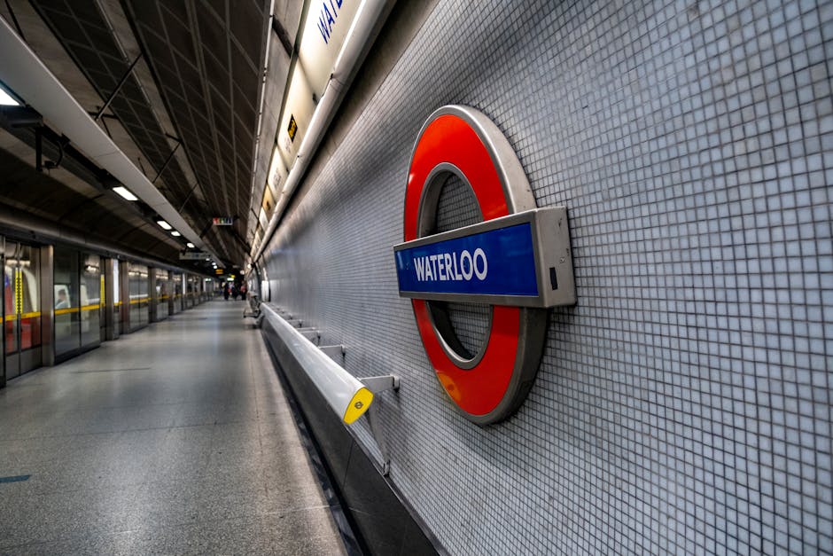 A London Underground station platform with seven seated passengers, some using mobile phones and one wearing a striped shirt, is visible alongside a moving train with a red, white, and blue exterior. 
